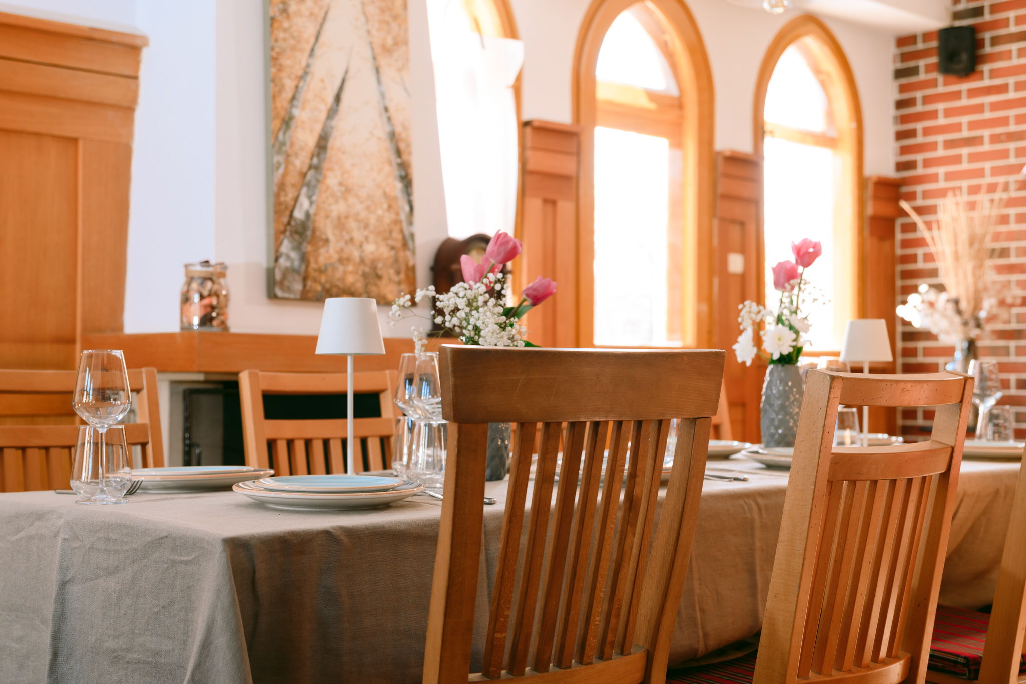 Idee - eveniment perfect Buongiorno 1 - Buongiorno Italian Sunlit restaurant dining area with wood chairs, a flower centerpiece, and glassware on a table. Behind are arched windows and brick walls.