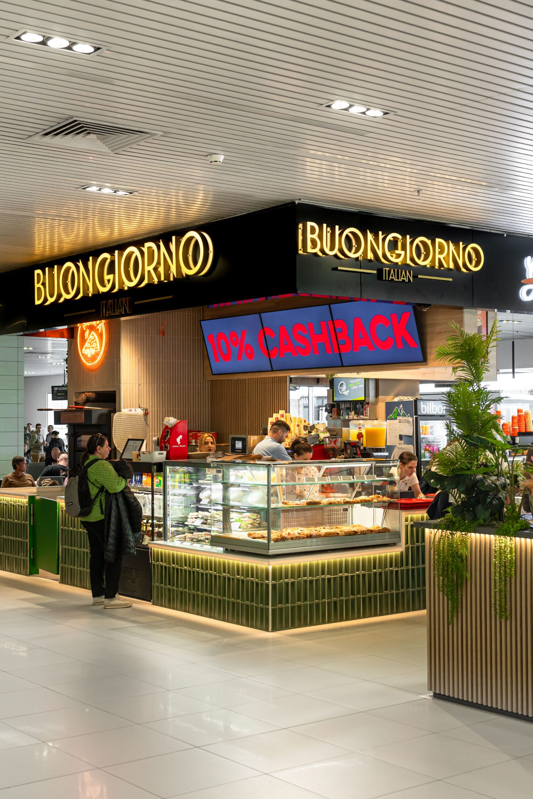 Italian cafe counter inside a mall, Buongiorno Italian with a glass pastry display and customers ordering at the counter, 10% CASHBACK sign visible above the counter