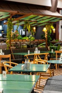 Indoor restaurant seating with green tables, wooden chairs, and hanging plants.