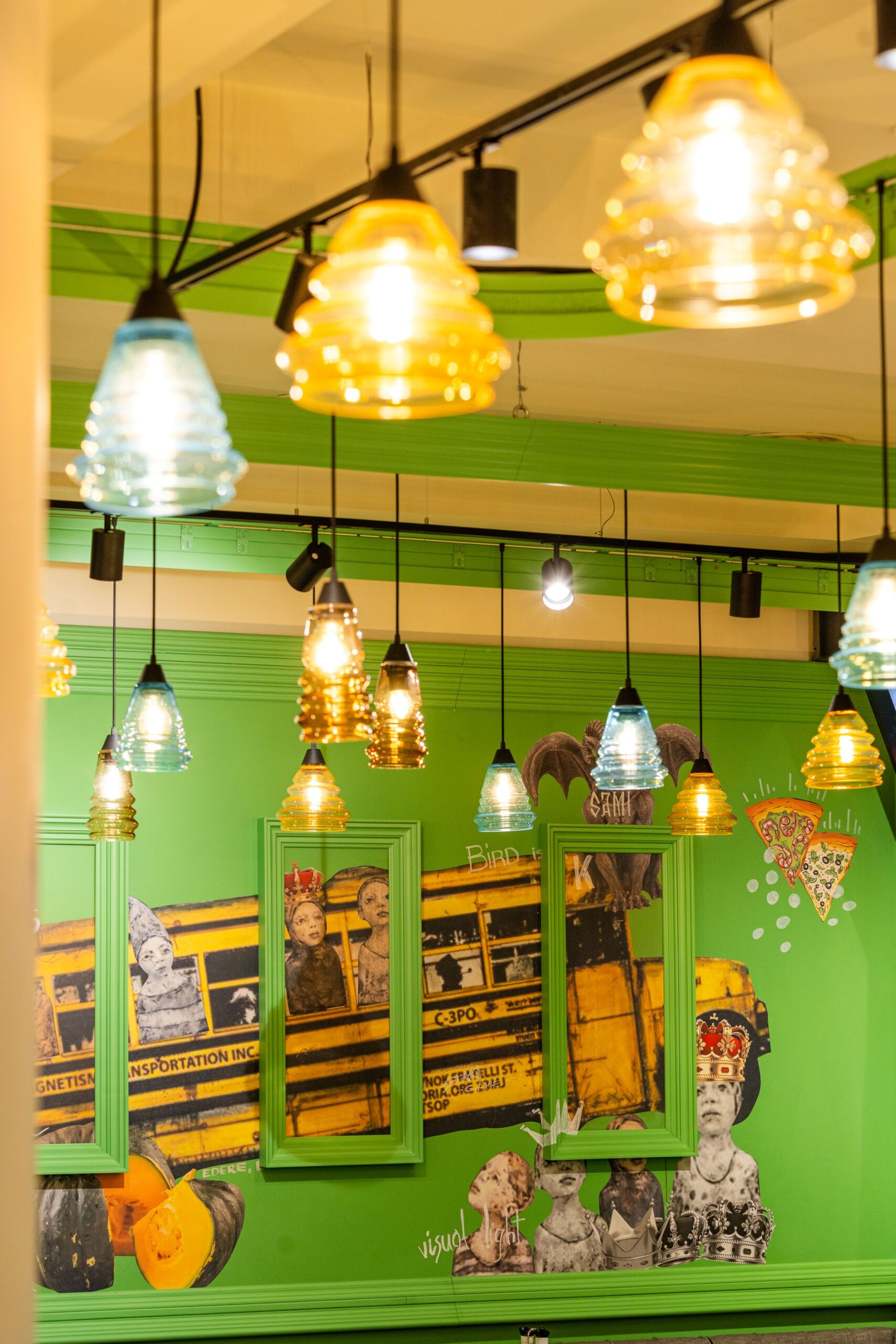 Colorful glass pendant lights glow above a lime-green wall decorated with framed vintage posters and crown illustrations.