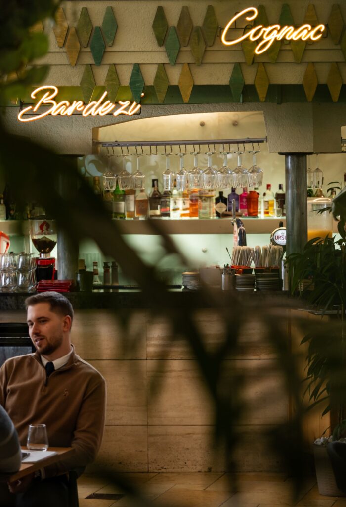 bg victoriei-10 - Buongiorno Italian Bar interior with hanging glasses, backlit liquor shelf, and a man seated at a table beneath neon signs.