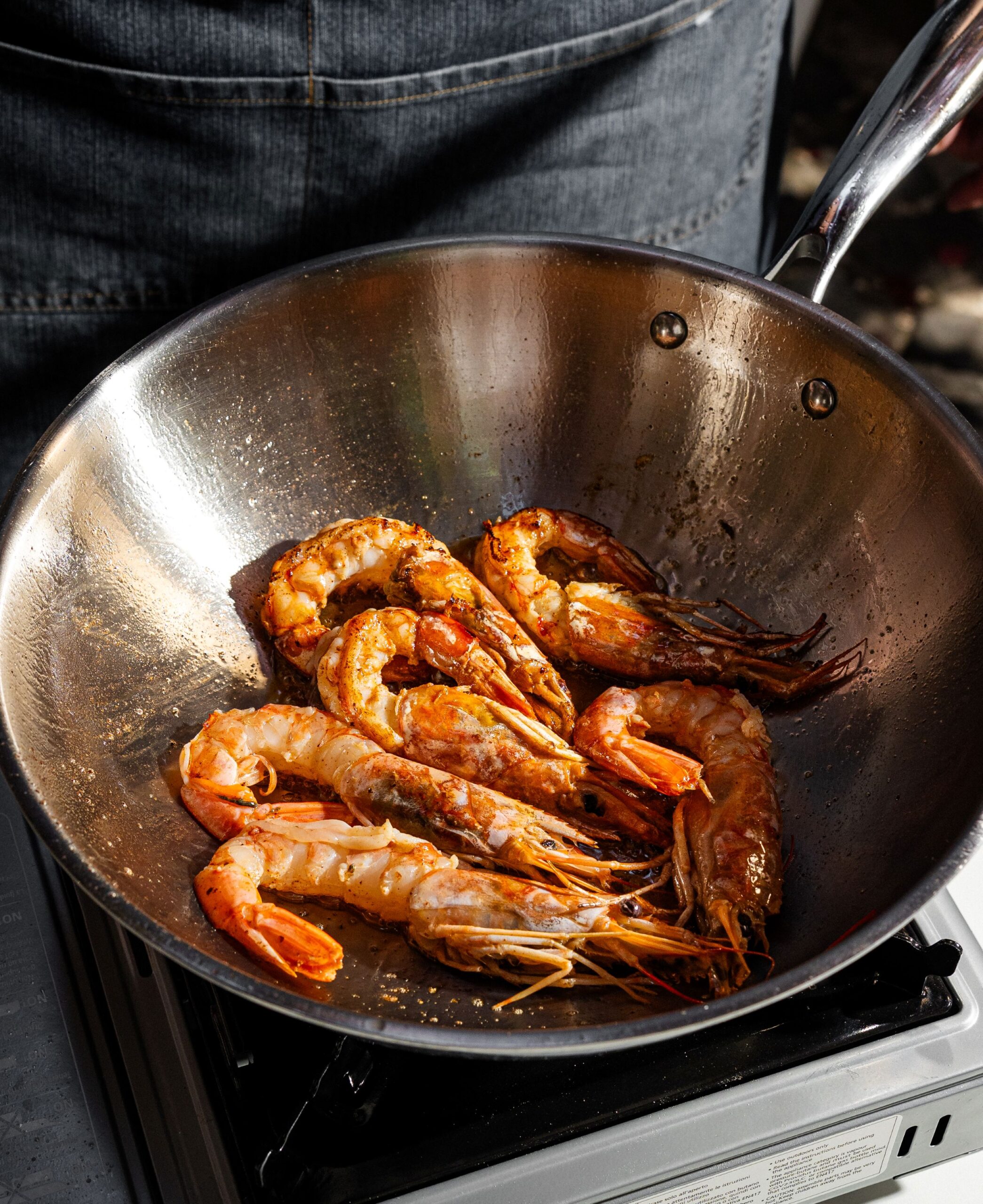 buongiorno-11 - Buongiorno Italian Close-up of a skillet filled with cooked shrimp with orange-pink shells in oil on a stove edge, ready to serve in a pan
