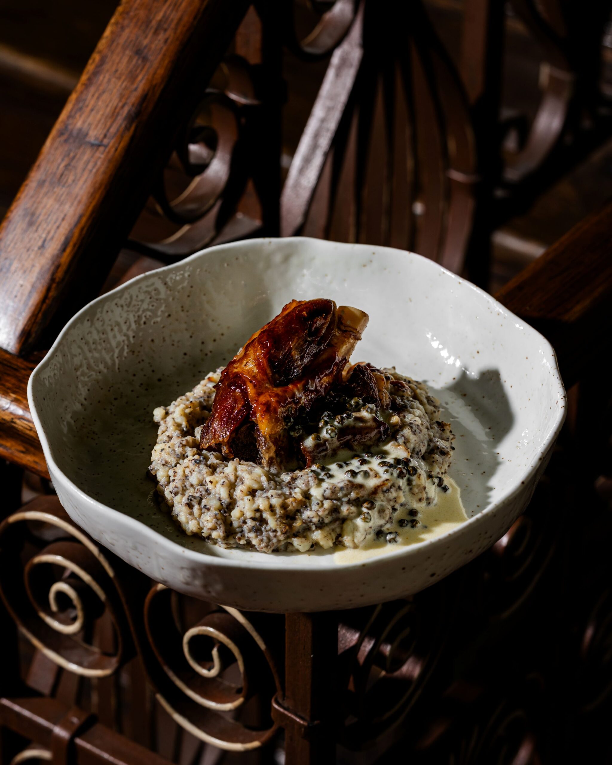 buongiorno-37 - Buongiorno Italian White ceramic bowl filled with creamy oatmeal and seeds, topped with a glazed roasted chicken wing on a dark wooden table.