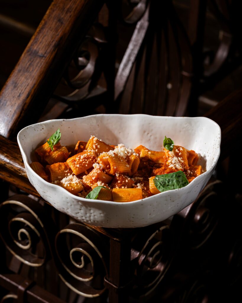 buongiorno-38 - Buongiorno Italian White ceramic bowl of penne pasta in tomato sauce, topped with grated cheese and basil on a rustic wooden table.