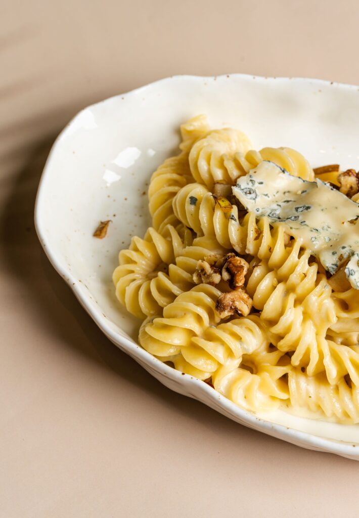 Creamy fusilli pasta with melted cheese and walnuts served on a white plate against a beige background