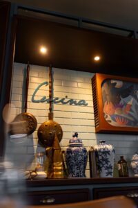 Display of copper pots hanging on a tiled wall above blue-and-white porcelain vases and a framed artwork in a cafe setting.