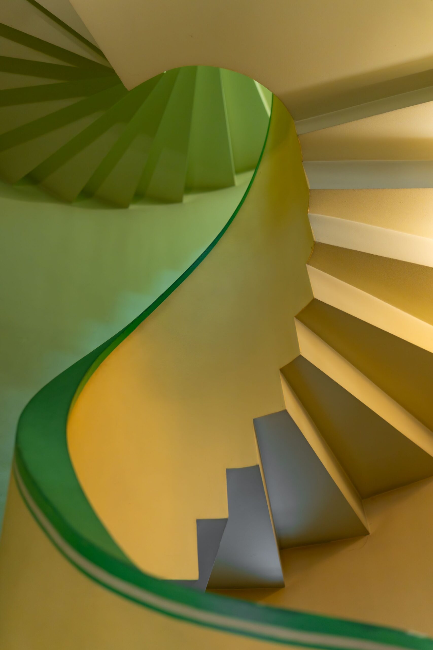 photo-31 - Buongiorno Italian Colorful spiral staircase viewed from above, with a green railing curling around yellow walls.