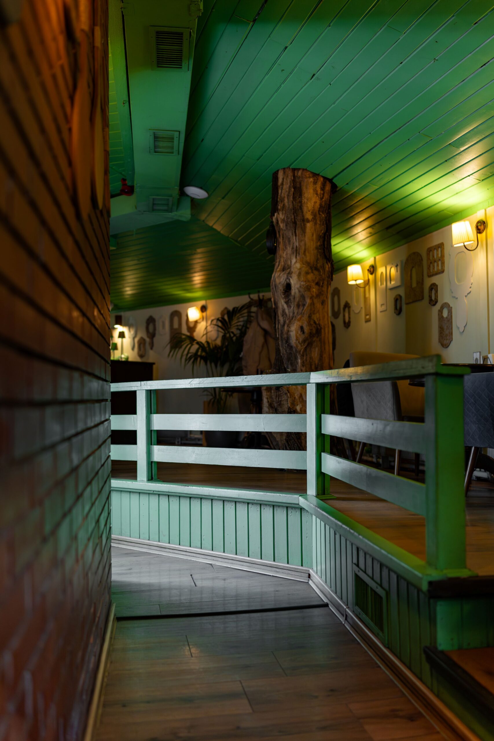 photo-34 - Buongiorno Italian Narrow indoor hallway with green paneled walls, a wooden trunk centerpiece, and warm wall lamps along a decorative wall display.