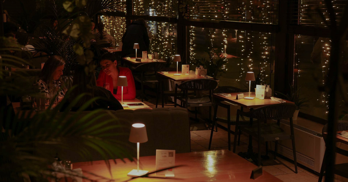 Ordinea felurilor la masă în Italia antipasti primi secondi dolce - Buongiorno Italian Dimly lit restaurant interior with warm string lights, several tables, and two women dining and chatting at a table.